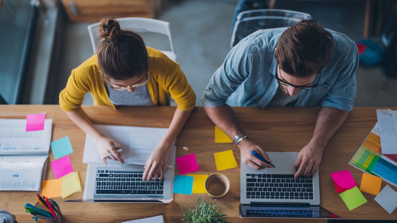 Content creator and SEO specialist collaborating at a desk with laptops and notes, emphasizing integrated content and SEO strategies.