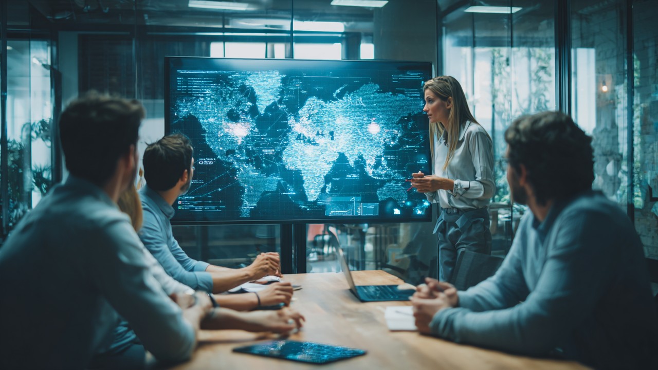 Digital marketing team analyzing global map on large screen, discussing multiregional content strategies in a modern office.