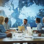 Diverse professionals collaborating around a digital map in a modern office, emphasizing teamwork and global strategy.