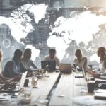 Diverse professionals collaborating around a modern office table with laptops, discussing global marketing strategies with world maps and charts displayed.