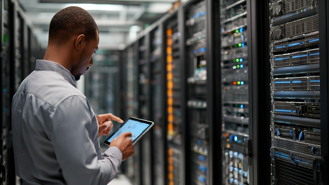 Server room with racks of servers and a technician monitoring performance metrics on a tablet, highlighting backend site speed optimization.