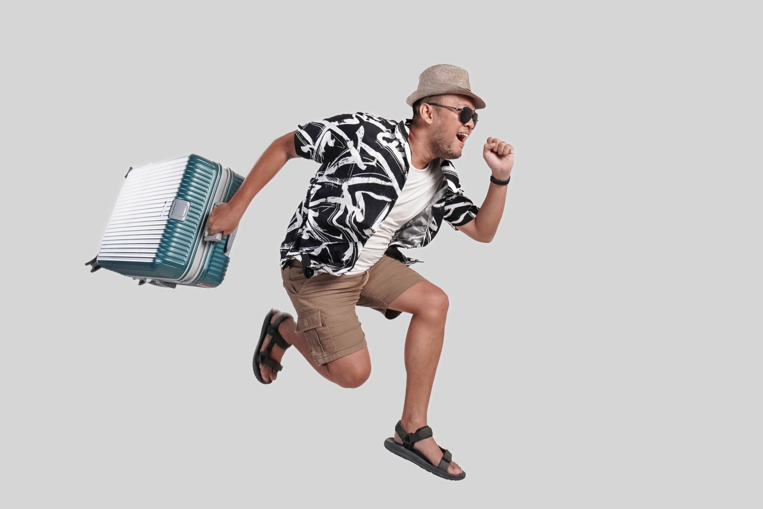 Cheerful young Asian man tourist jumping while bringing suitcase with an exciting smile.