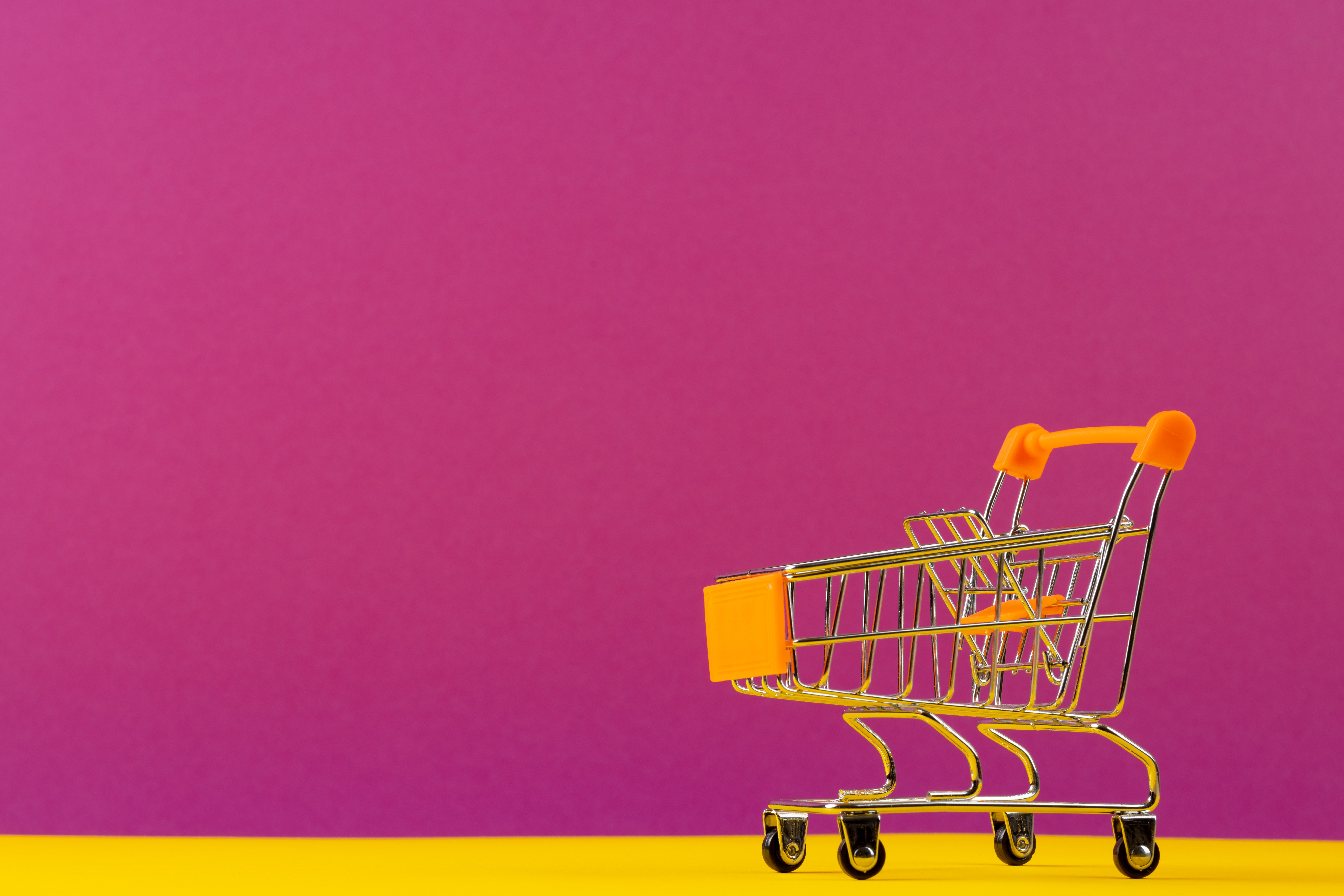 Composition of shopping cart on pink and yellow background